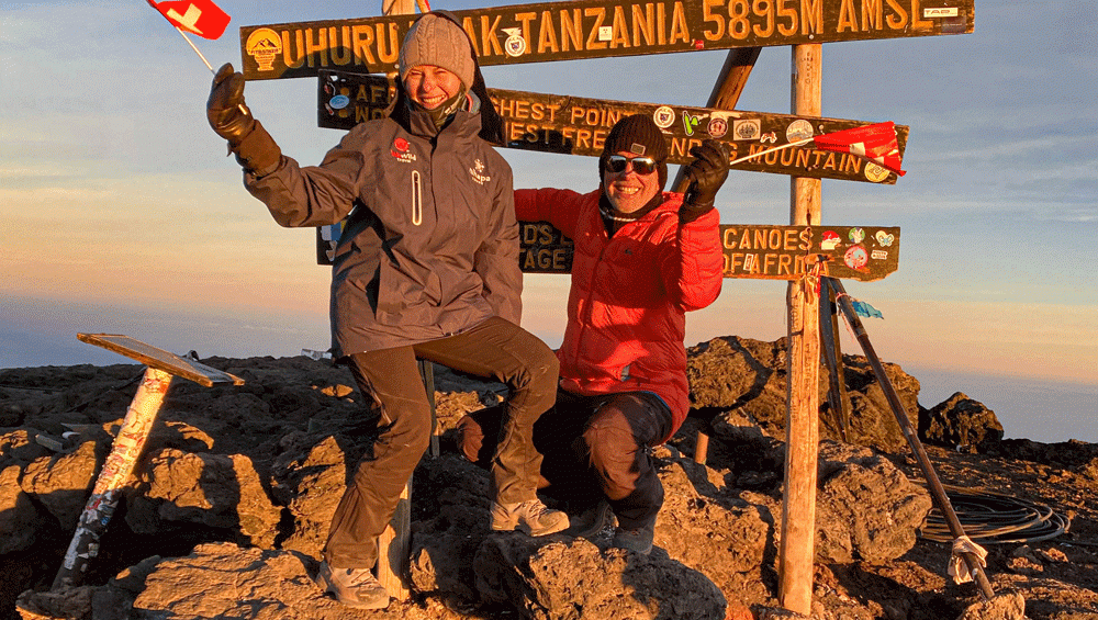 Trekkers standing at the wooden Uhuru Peak sign on the summit of Mount Kilimanjaro via the Rongai Route.