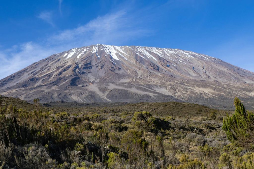 Mount Kilimanjaro snow-capped peak rising above clouds and African landscape.