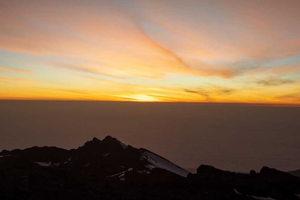 Mount Kilimanjaro summit Uhuru Peak above clouds with glacier and sunrise views.