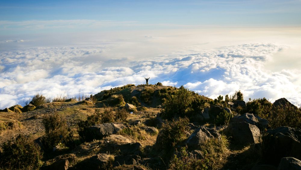 Mount Kilimanjaro under changing weather conditions with clouds surrounding the mountain and snow near the summit.