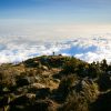 Mount Kilimanjaro under changing weather conditions with clouds surrounding the mountain and snow near the summit.