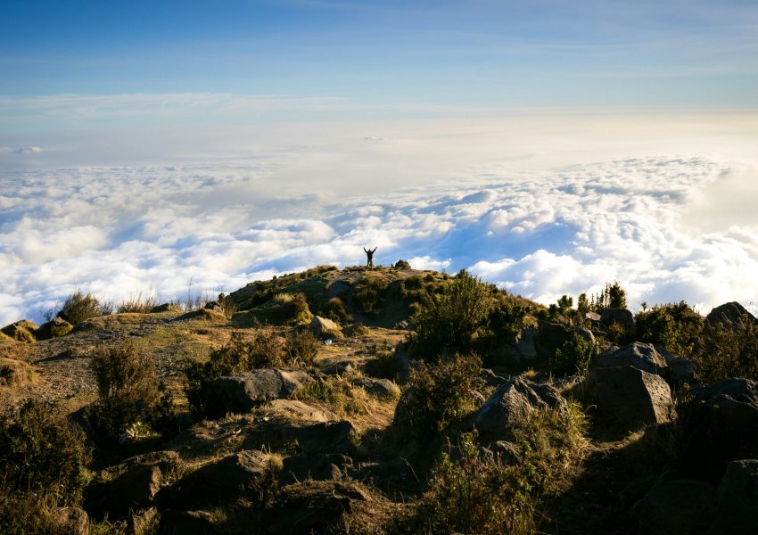 Mount Kilimanjaro under changing weather conditions with clouds surrounding the mountain and snow near the summit.