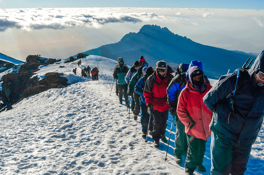 Climber standing at Uhuru Peak summit on Mount Kilimanjaro above Tanzania’s clouds