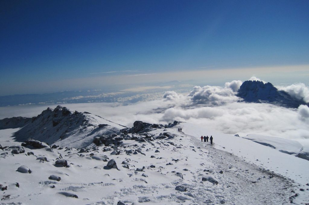 Climbers approaching Barafu Camp summit route through rocky terrain beneath Mount Kilimanjaro's high alpine slopes.
