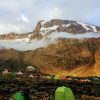 Mountain tents on Mount Kilimanjaro campsite beneath towering peaks, illustrating climbing Kilimanjaro cost and adventure planning.
