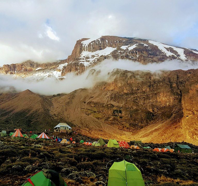 Mountain tents on Mount Kilimanjaro campsite beneath towering peaks, illustrating climbing Kilimanjaro cost and adventure planning.