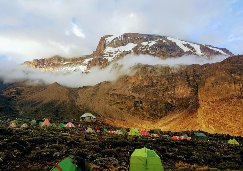 Mountain tents on Mount Kilimanjaro campsite beneath towering peaks, illustrating climbing Kilimanjaro cost and adventure planning.