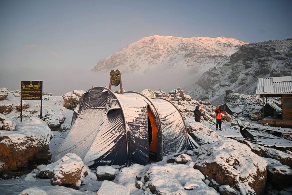 Snow-covered tents at Barafu Camp on Mount Kilimanjaro surrounded by rocky terrain before summit night.
