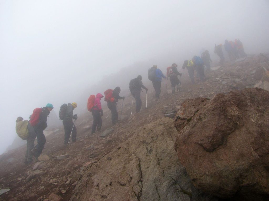 Climbers ascending Mount Kilimanjaro during the rainy season on muddy and mist-covered mountain trails