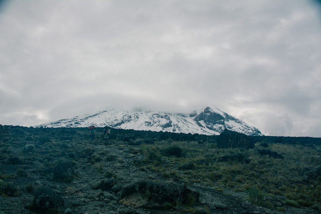 Mount Kilimanjaro rising above clouds with glaciers, rugged slopes, and stunning summit views.
