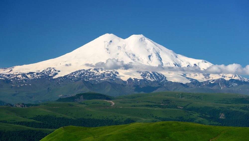 Mount Elbrus snow-covered twin peaks rising above Caucasus Mountains with dramatic alpine landscape in Russia.