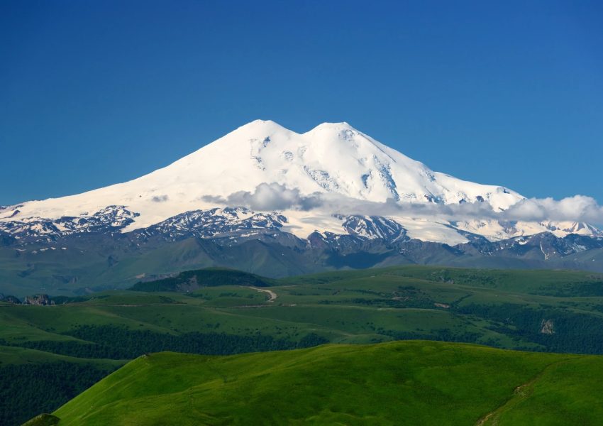 Mount Elbrus snow-covered twin peaks rising above Caucasus Mountains with dramatic alpine landscape in Russia.