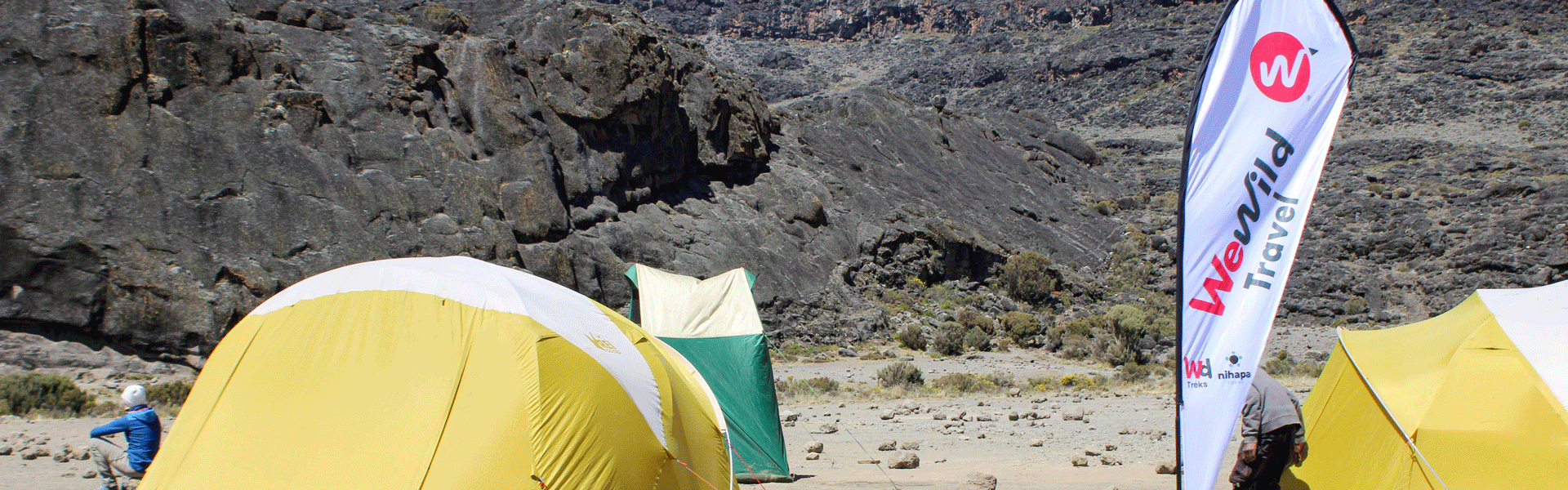 A trekker resting at an Umbwe Route campsite on Mount Kilimanjaro, surrounded by mountain tents and camping equipment.
